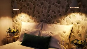 Ein ordentlich bezogenes Bett mit einem grünen Kopfkissen, zwei Nachttische mit Lampen und floralem Wandpapier.