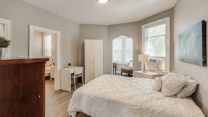 A bedroom with a bed, a desk, a chair, and a dresser.