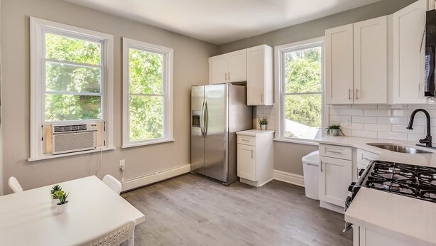 A modern kitchen with white cabinetry, a stainless steel refrigerator, a gas stove, and a window overlooking greenery.