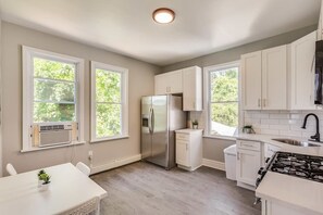 A modern kitchen with white cabinetry, a stainless steel refrigerator, a gas stove, and a window overlooking greenery.