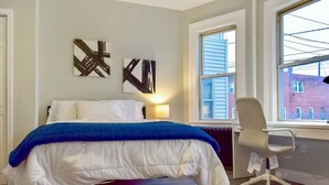 A bedroom with a bed, a desk, and two abstract paintings on the wall.