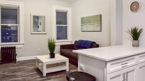 A modern living room with a white sofa, a small coffee table, a white kitchen counter, and a radiator.