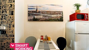 A compact kitchen with a microwave on top of a fridge, a table with a striped tablecloth, and a cityscape painting on the wall. - La Casa di Mattoni by Wonderful Italy (Torino)
