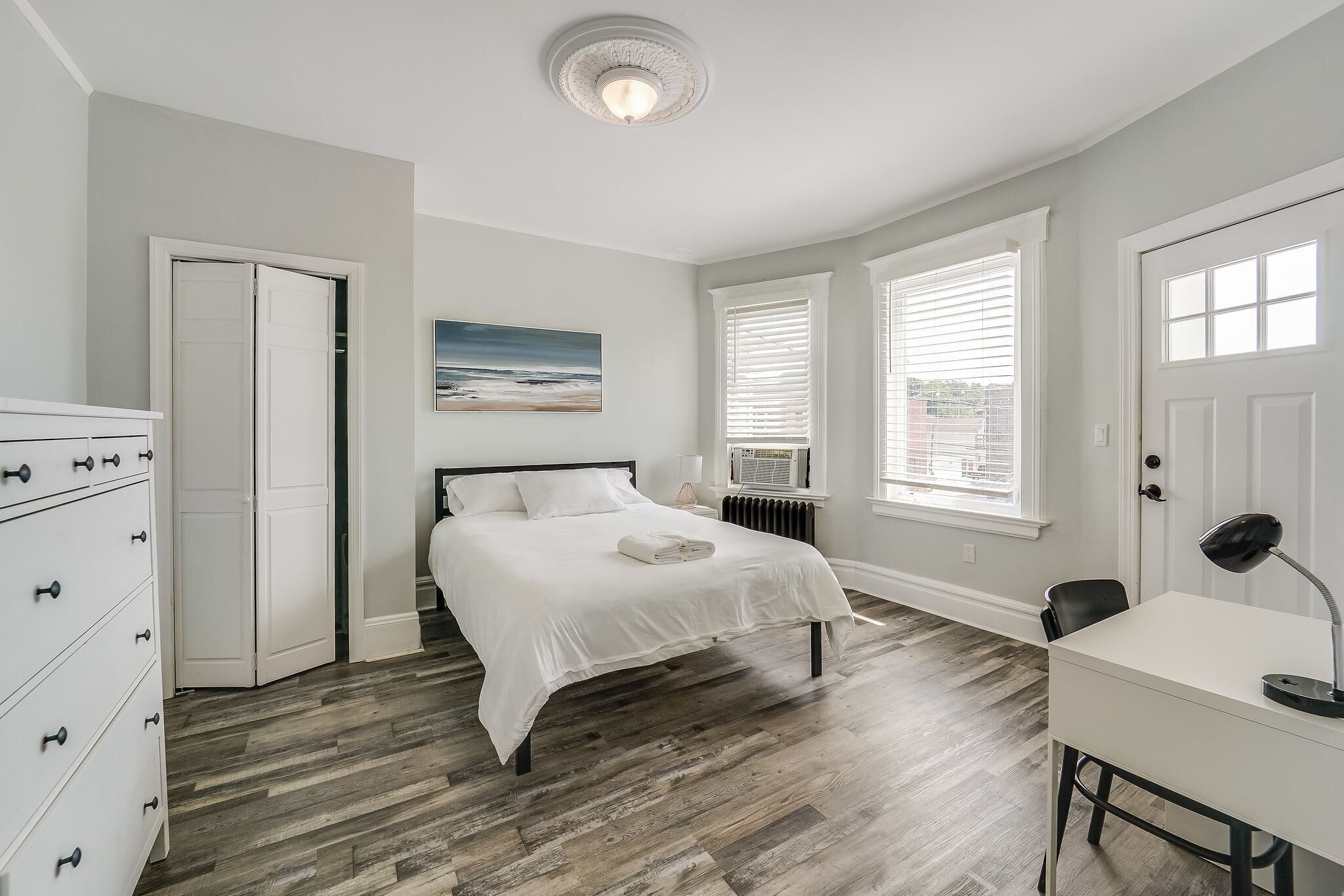 Une chambre à coucher avec un lit, une commode, un bureau et des fenêtres.