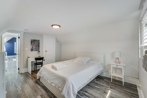 A bedroom with a bed, a desk, a chair, a map on the wall, and a door leading to another room.