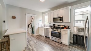 A modern kitchen with white cabinets, a stainless steel range, a microwave, and a window providing natural light. - 4BR/2BA Duplex Apt in Downtown Montclair w/Parking (Montclair)