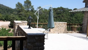 Une terrasse en pierre avec une table et des chaises, un parasol suspendu et une lanterne.