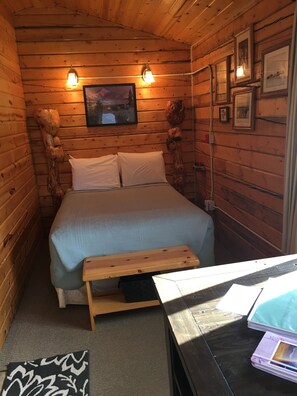 A wooden cabin room with a bed, two wall-mounted lights, and framed pictures. - Earthsong Lodge - STAND (Healy)