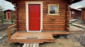 Punaisella ovella varustettu hirsihökkelö, jossa on nimikyltti, jossa lukee »ATHABASCAN», ja pieni ikkuna.
