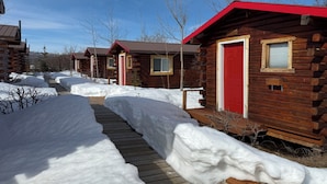 A row of log cabins with red doors and windows, surrounded by snow-covered ground and a wooden walkway. - Earthsong Lodge - FAMLY (Healy)