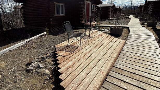 A wooden deck leading to log cabins with a clear sky. - Earthsong Lodge -Two Room Cabin (Healy)