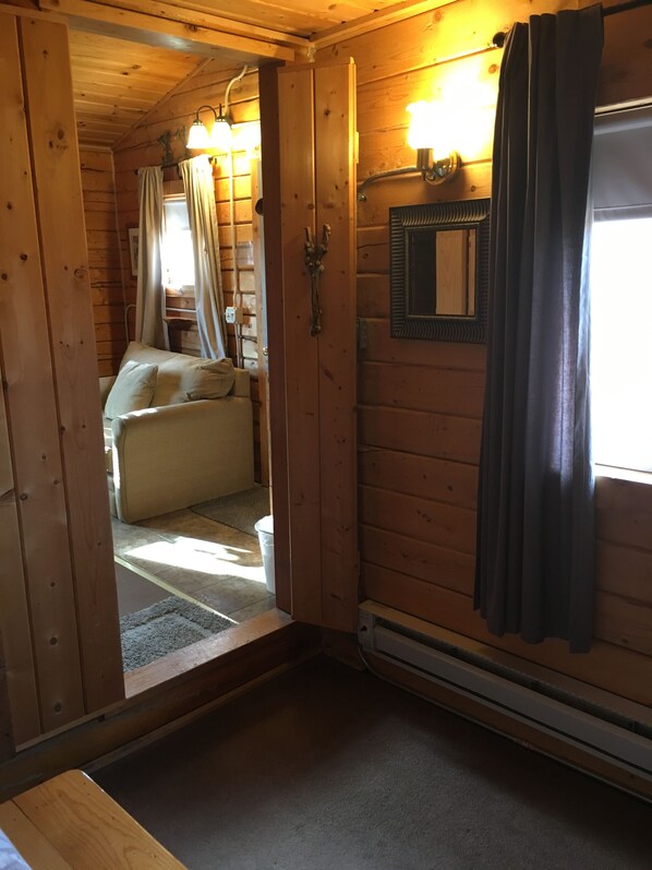 L’intérieur d’une cabane en bois, avec un lit, un miroir et une fenêtre avec des rideaux.