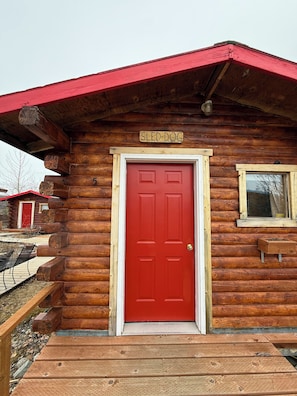 A red door with a sign above it reading 'SLED DOG' and a window to the right.
