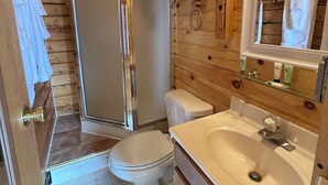 Et badeværelse i en træhytte med bruser, toilet og håndvask.