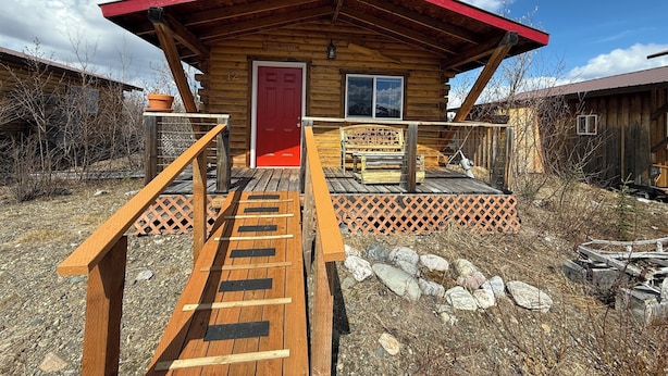 Une cabane en bois avec une porte rouge, une véranda en bois et une enseigne sur laquelle on peut lire : « House Pilot ».