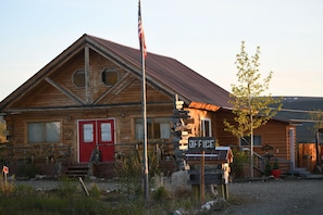 A rustic log cabin with a red door, a sign indicating an office, and a flagpole with an American flag.