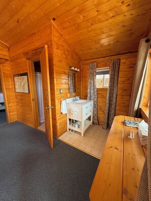 A wooden cabin interior with a bathroom, a wooden desk, and a window with curtains. - Earthsong Lodge - Two Bedroom Cabin (Healy)