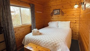 Une pièce de cabane en bois comprenant un lit, un banc, une fenêtre et une porte.