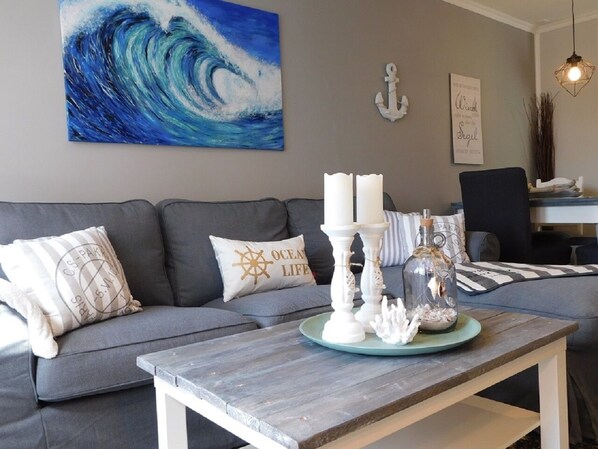 A living room with a grey sofa, a coffee table with candles and a glass jar, and a painting of a wave on the wall.