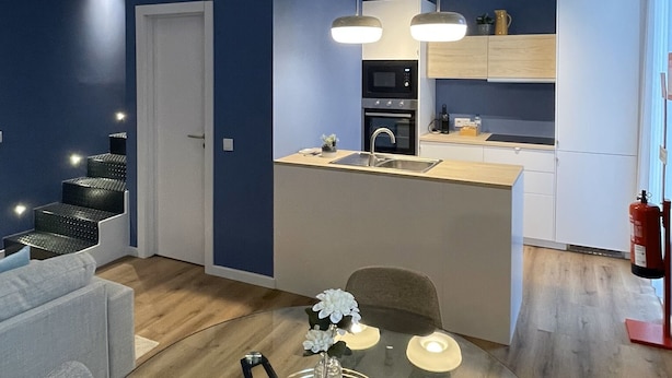 A modern living space with a glass dining table, a sofa, and a kitchen area with a microwave and stove. - MyTrip Porto (Matosinhos)