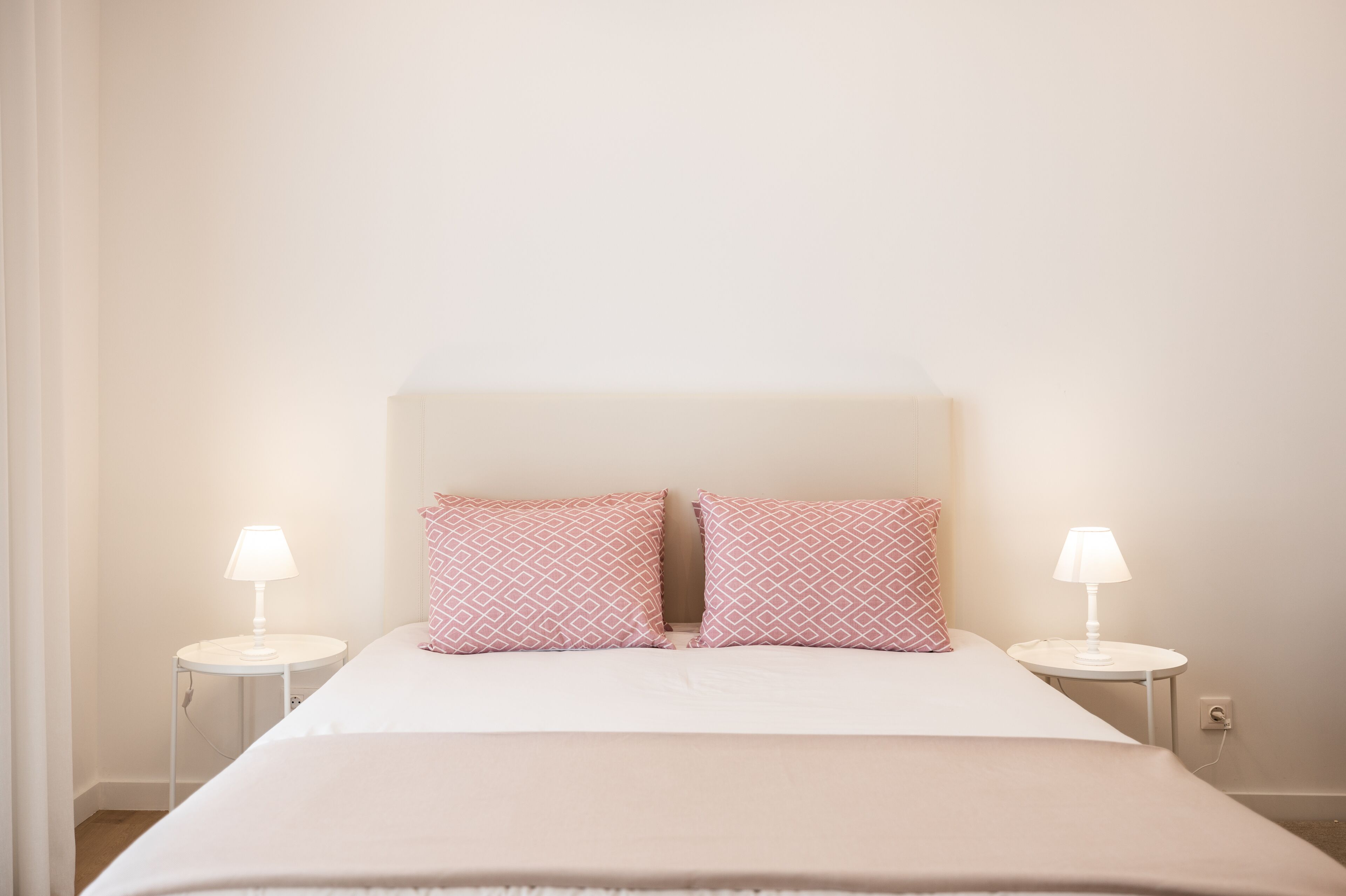 Un lit bien fait, avec deux oreillers, deux tables de chevet avec des lampes et un mur sobre.