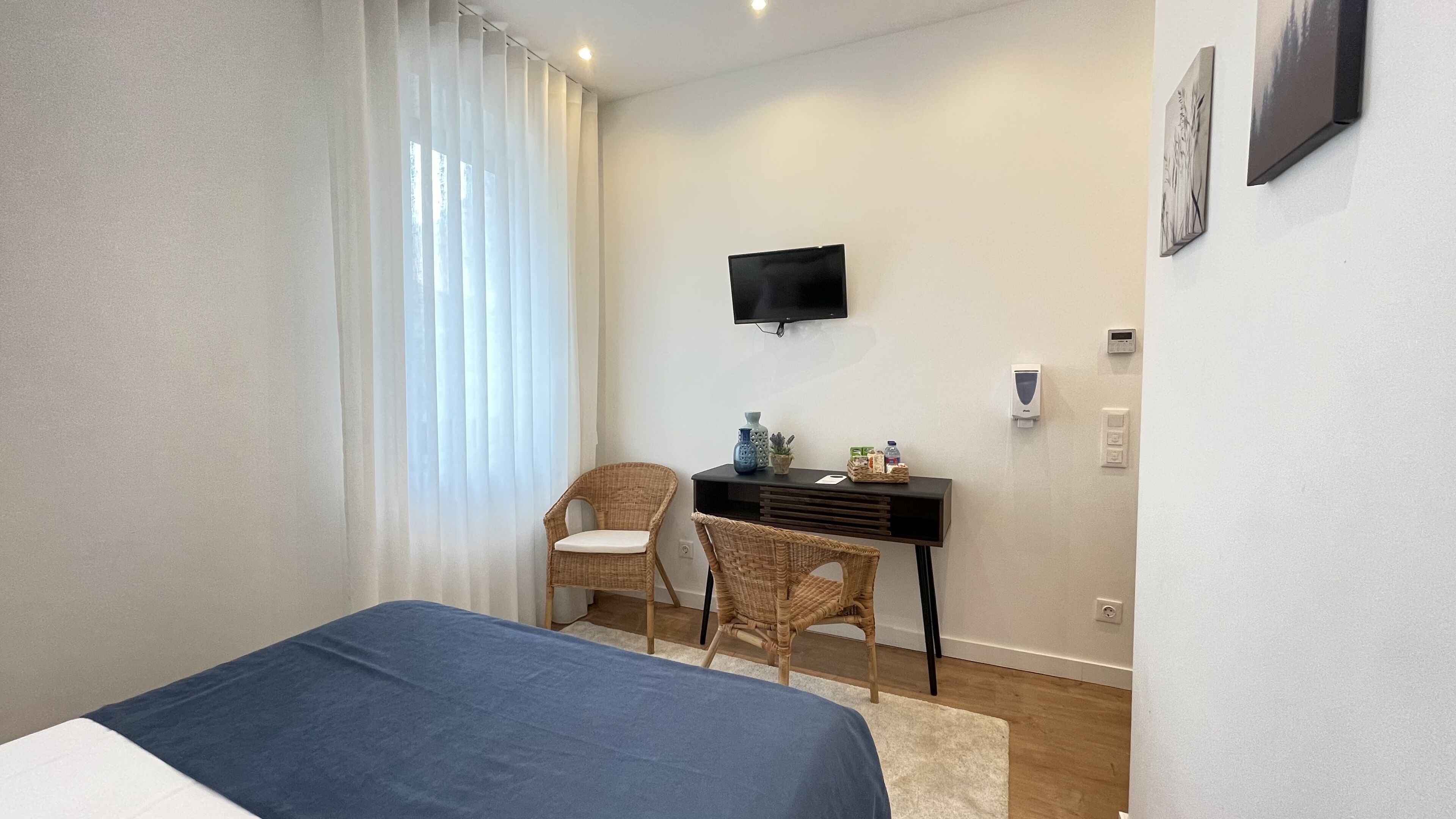 A bedroom with a bed, a desk, a chair, a TV, and a window with curtains.