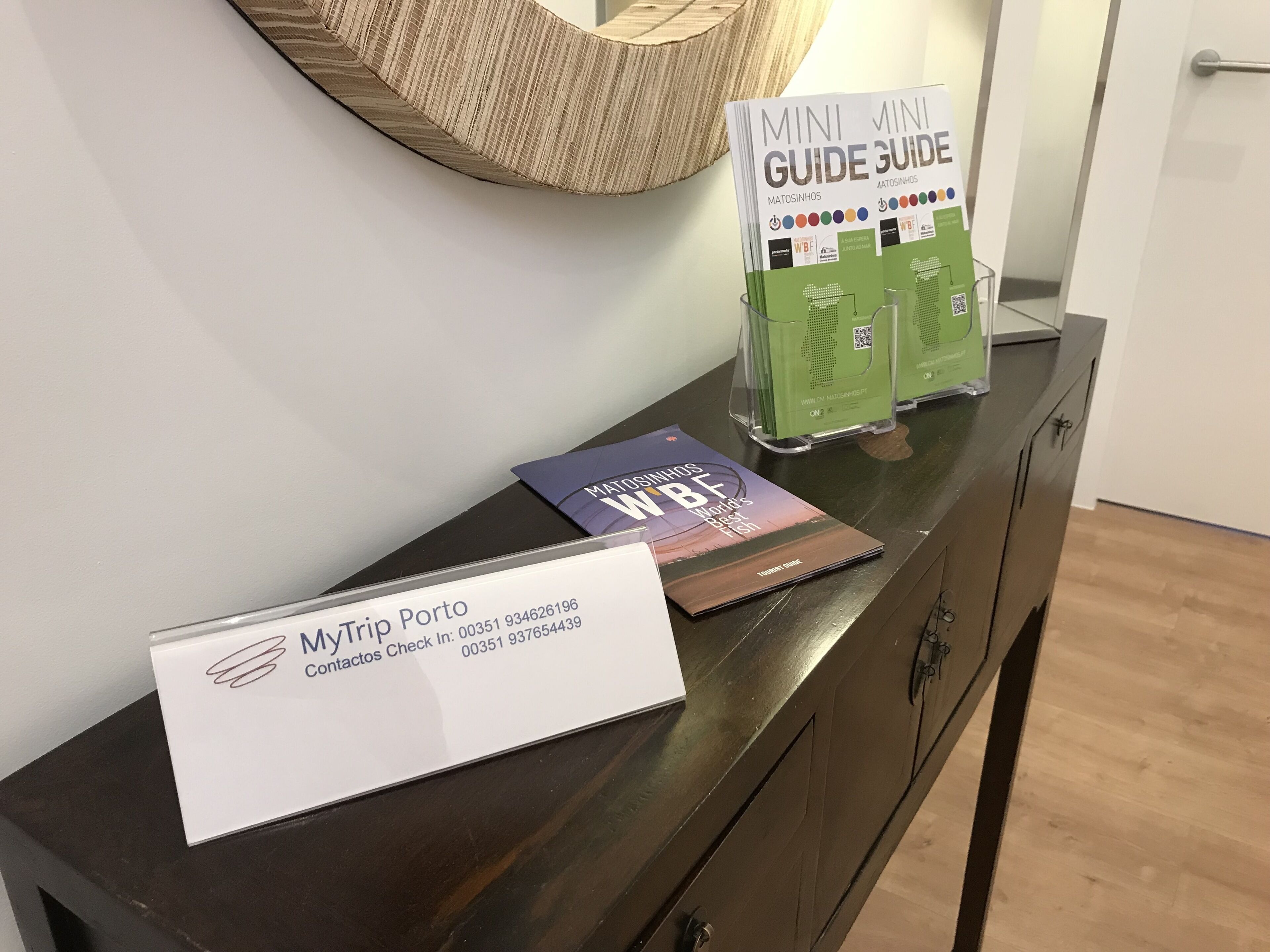 A reception desk with a sign for MyTrip Porto, a guidebook, and a green information kiosk.