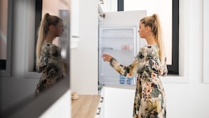 A woman in a floral dress opening a modern, white-framed refrigerator in a kitchen with a window. - MyTrip Porto (Matosinhos)