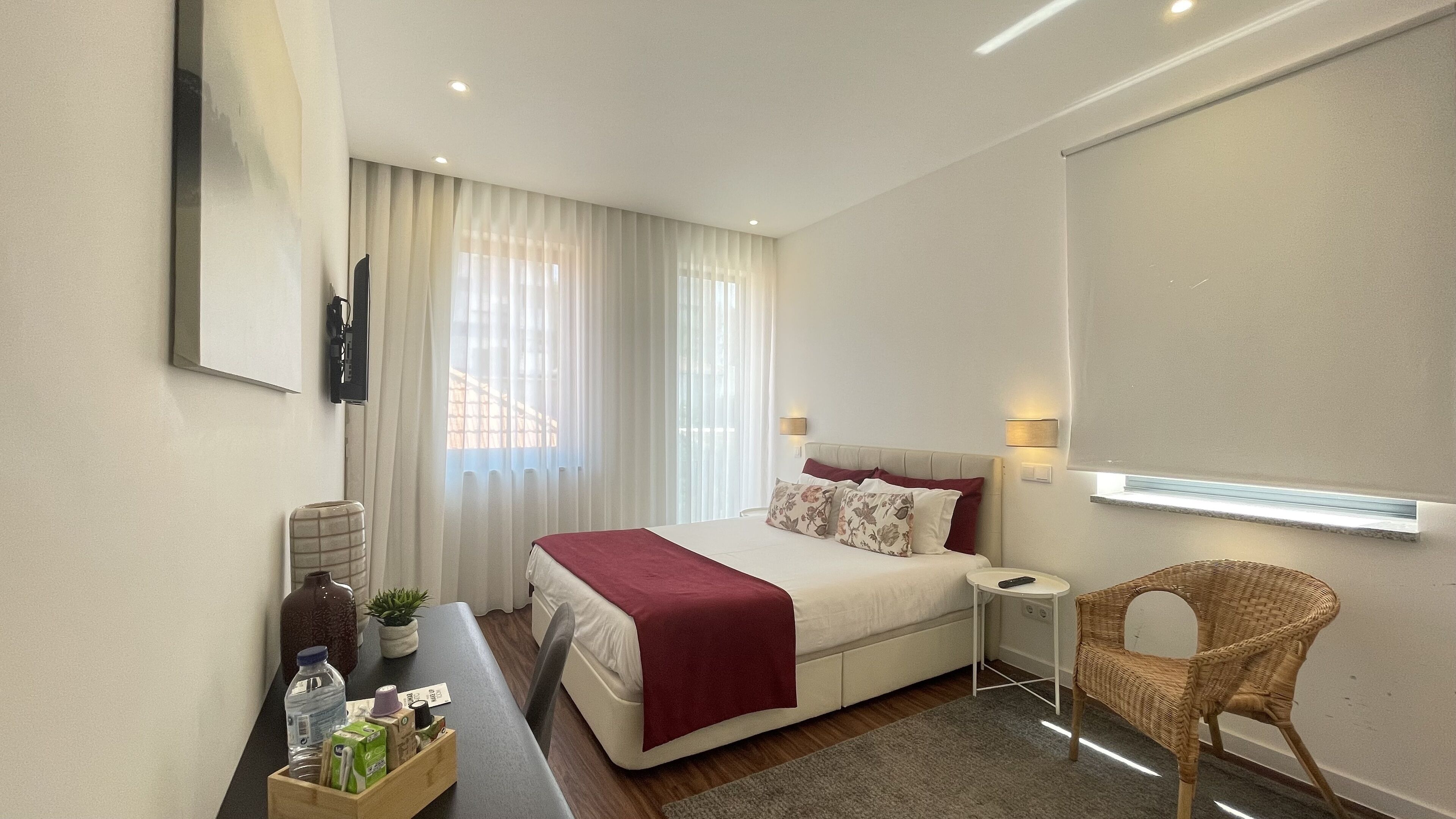 Habitació d'hotel moderna amb llit, tauleta de nit, cadira i una finestra gran amb cortines.