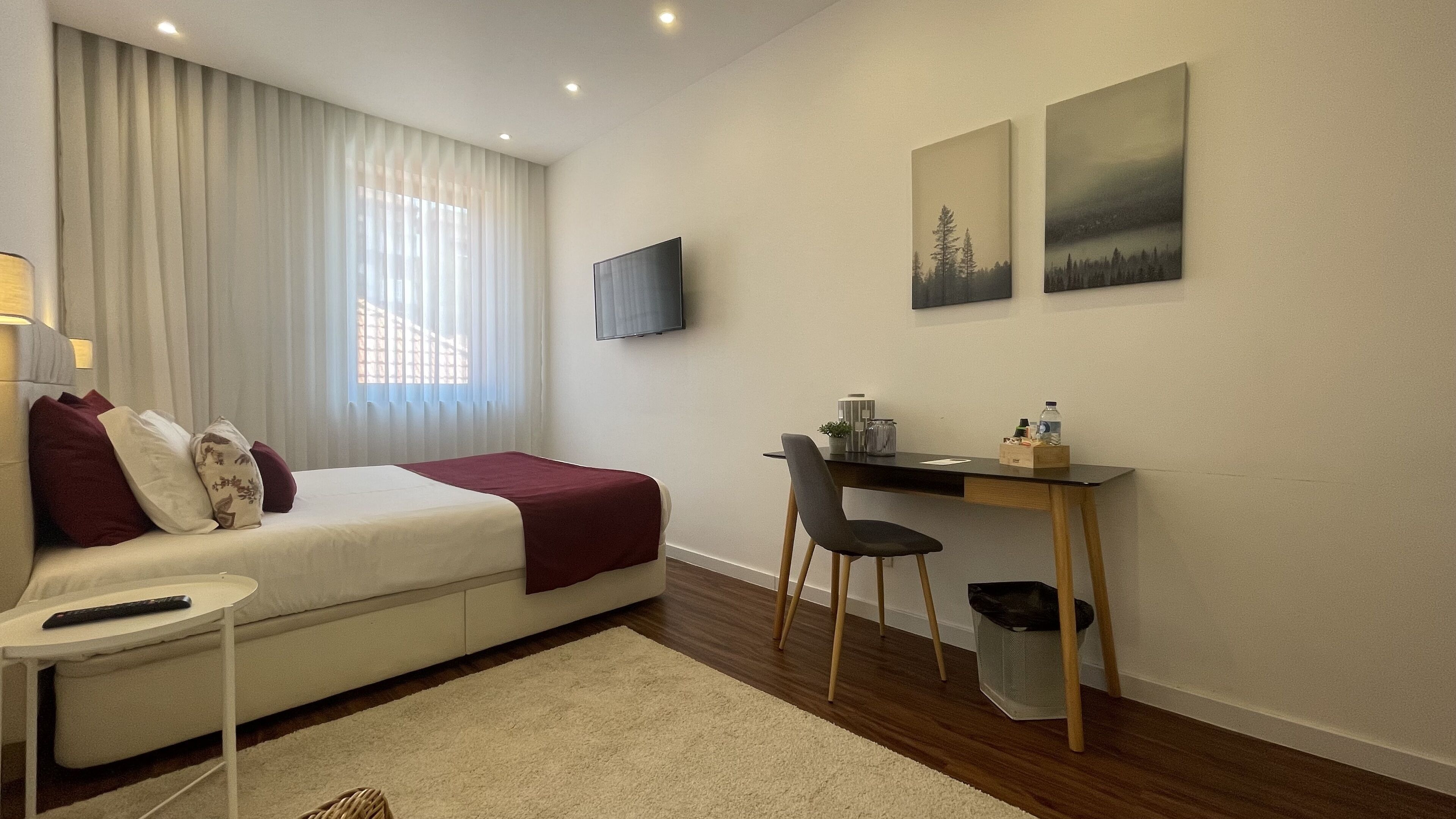 A hotel room with a bed, a desk, a chair, a TV, and two paintings on the wall.