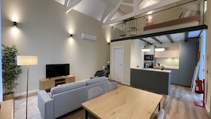A modern living room with a sofa, TV, and dining table. A kitchen is visible in the background. - MyTrip Porto (Matosinhos)