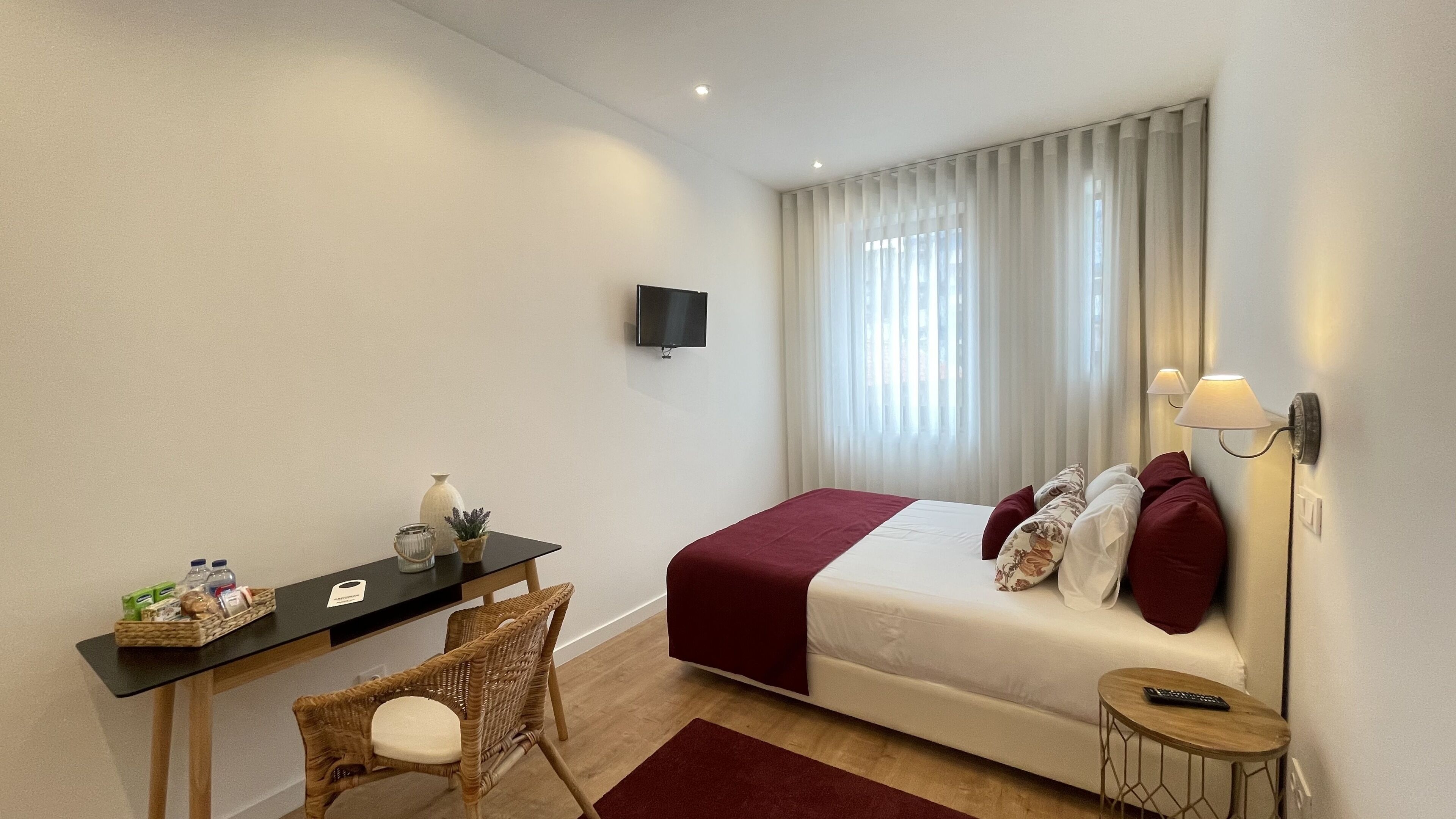 Une chambre d’hôtel avec un lit, un bureau, une chaise, une télévision et une fenêtre avec des rideaux.
