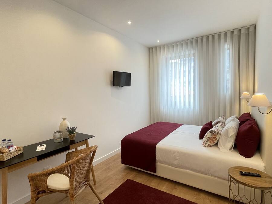 Habitación de hotel con cama, escritorio, silla, televisor y ventana con cortinas.