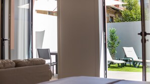 A hotel room with a bed, a chair, and a view of an outdoor area with lounge chairs and a small garden. - MyTrip Porto (Matosinhos)