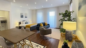 A modern hotel room with a bed, a sofa, a dining table, and a small seating area. - MyTrip Porto (Matosinhos)