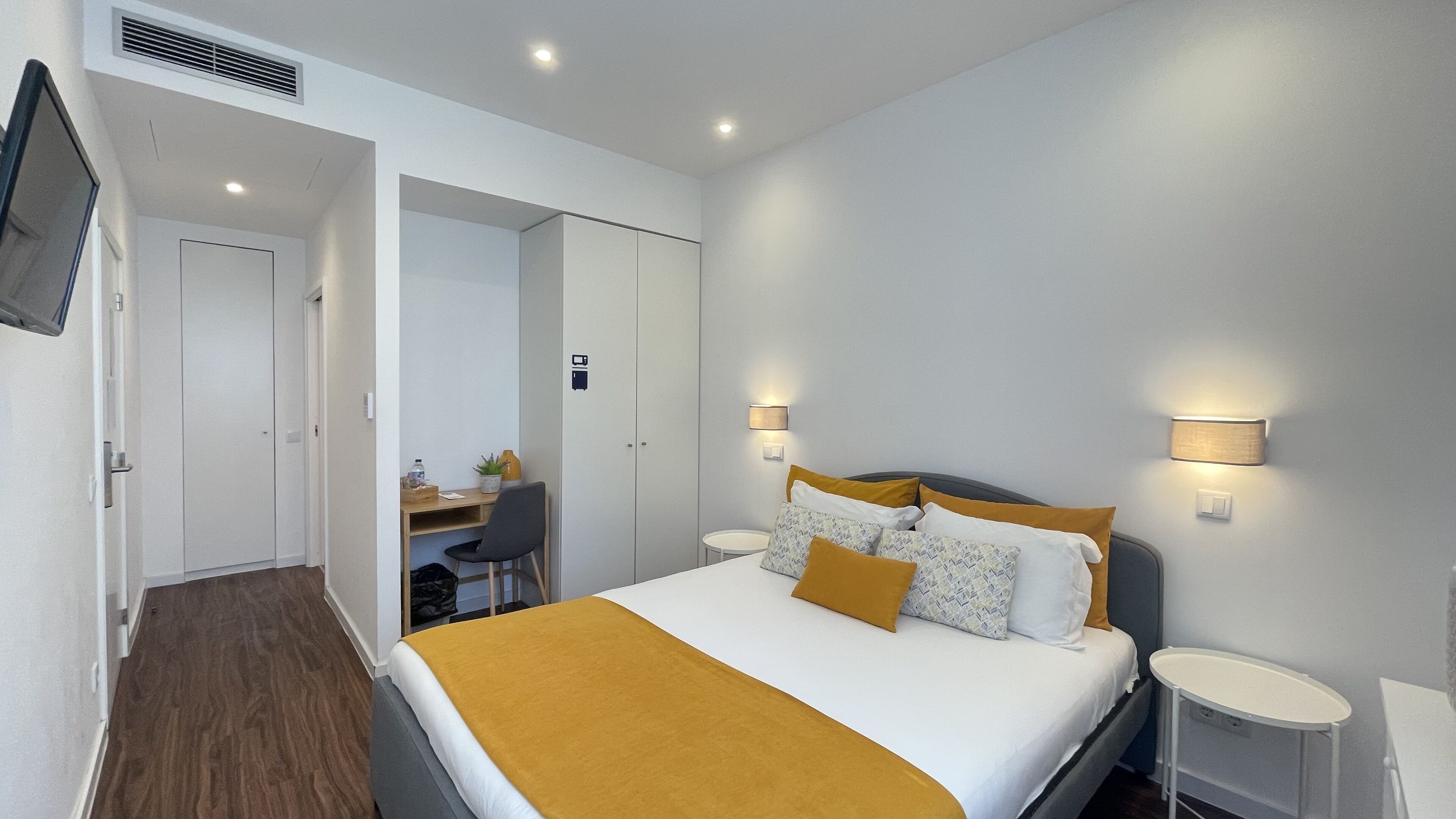 A modern hotel room with a bed, bedside tables, a desk, and a chair.