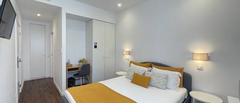 A modern hotel room with a bed, bedside tables, a desk, and a chair.
