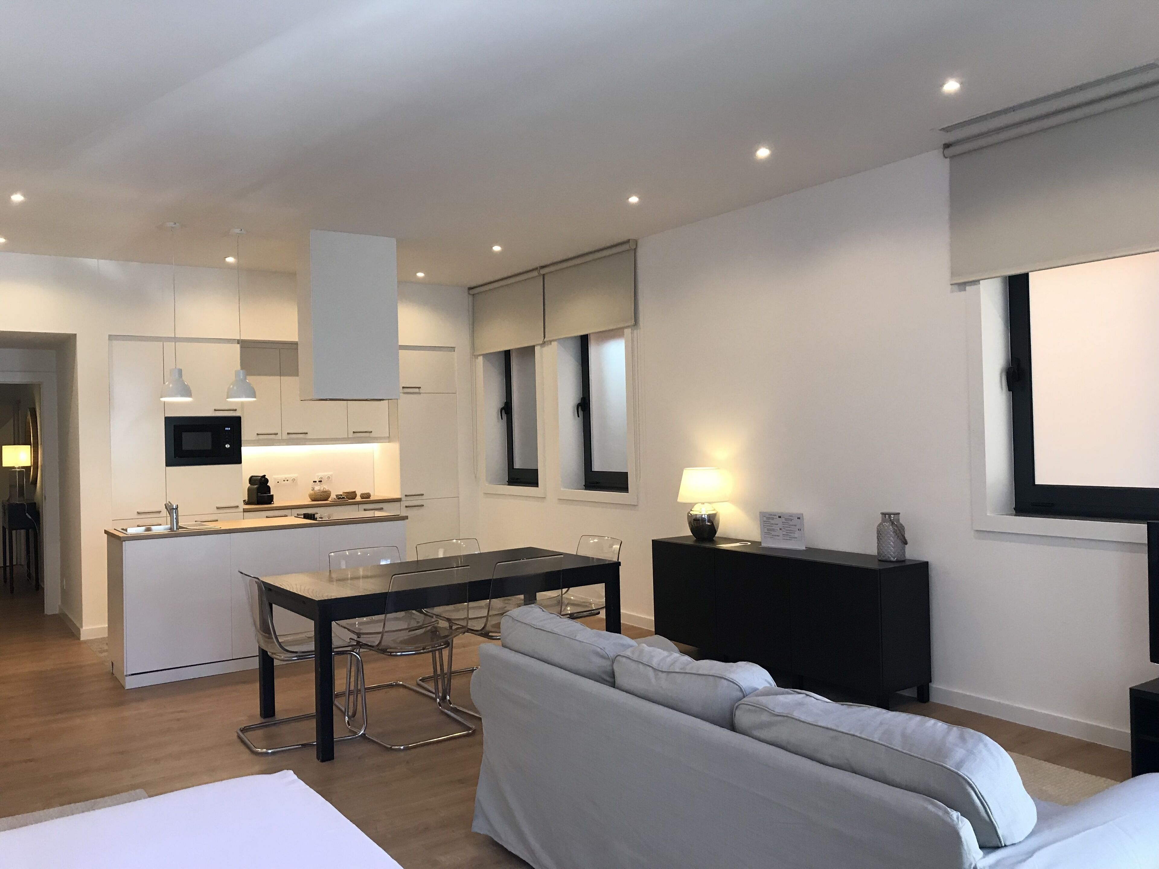 Een moderne, goed verlichte woonkamer met een bank, een eettafel en een keuken op de achtergrond.
