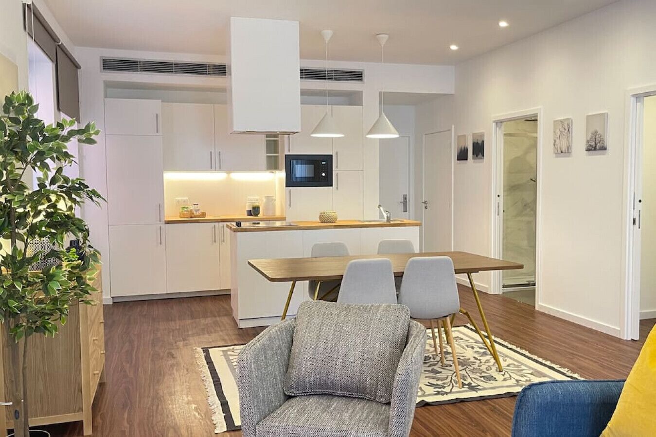 A modern kitchen with white cabinets, a wooden dining table, and a built-in TV.