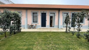 A two-story building with a tiled roof, a small patio with a table and chairs, and a well-maintained lawn. - MyTrip Porto (Matosinhos)