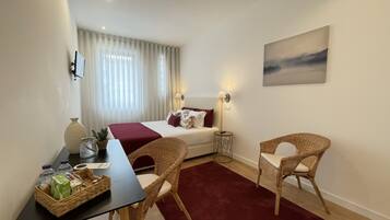 A hotel room with a bed, two wicker chairs, a table with breakfast items, a vase, and a painting on the wall.