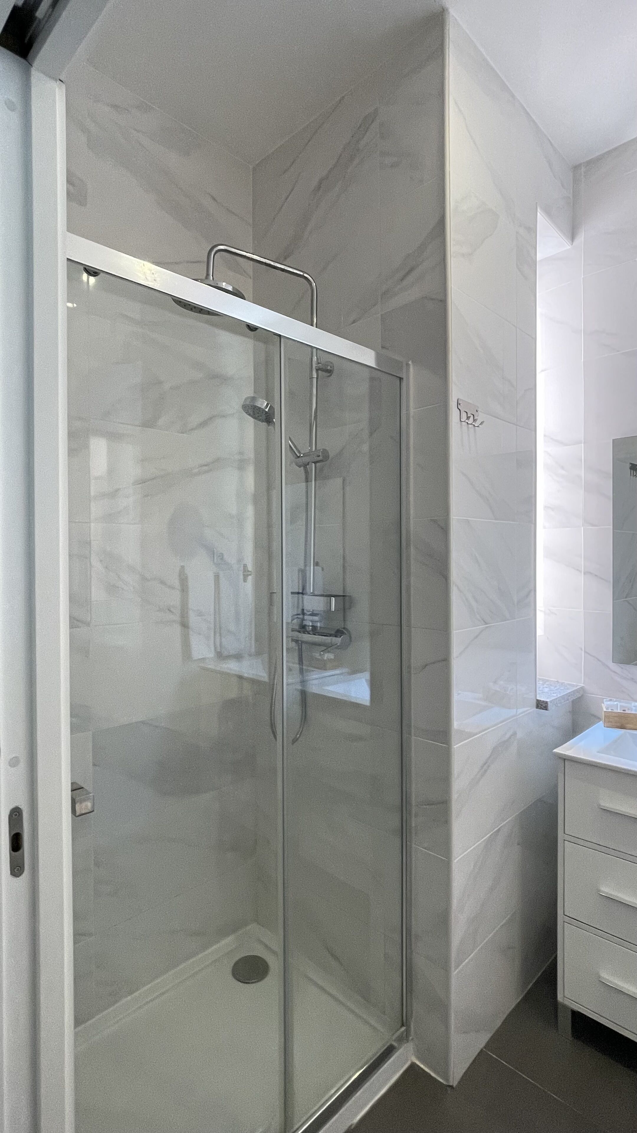 Un bagno moderno con cabina doccia in vetro, pareti in marmo e mobile lavabo bianco con cassetti.