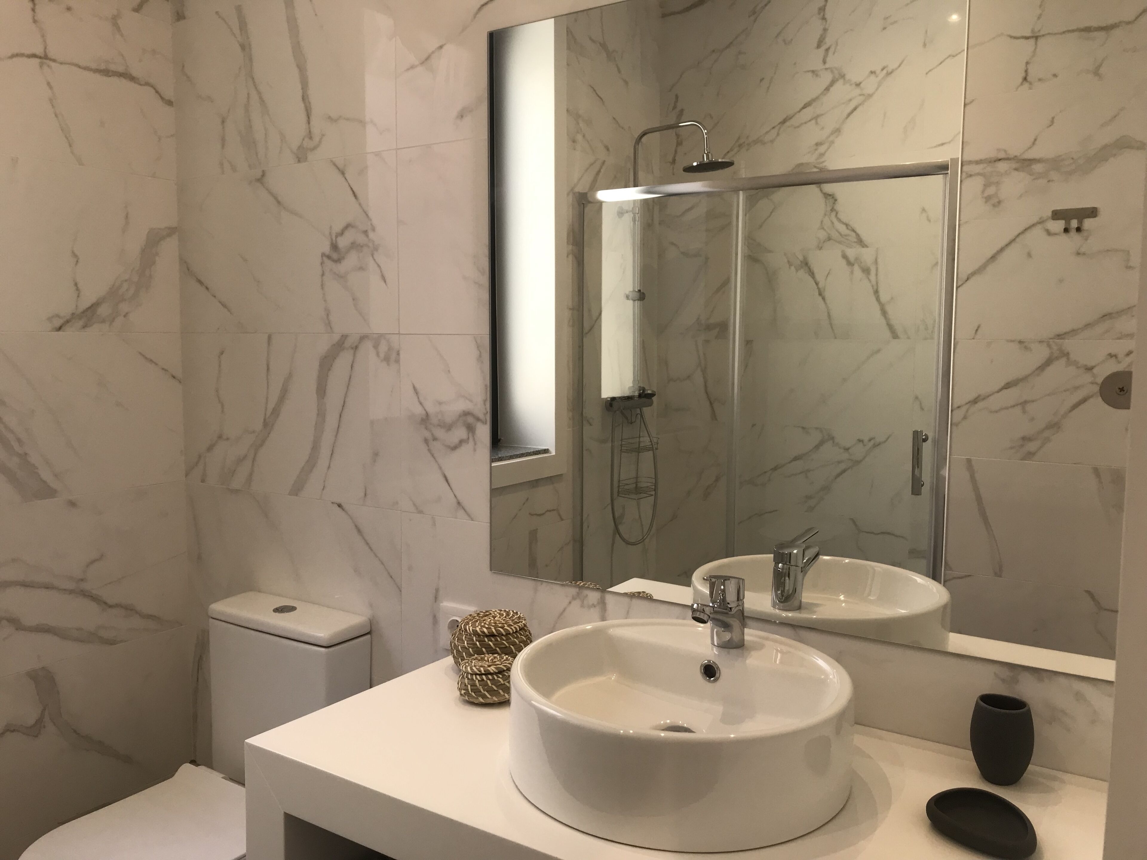 Un baño moderno con salpicadero de mármol, un lavabo redondo, un cabezal de ducha de mano y un inodoro.