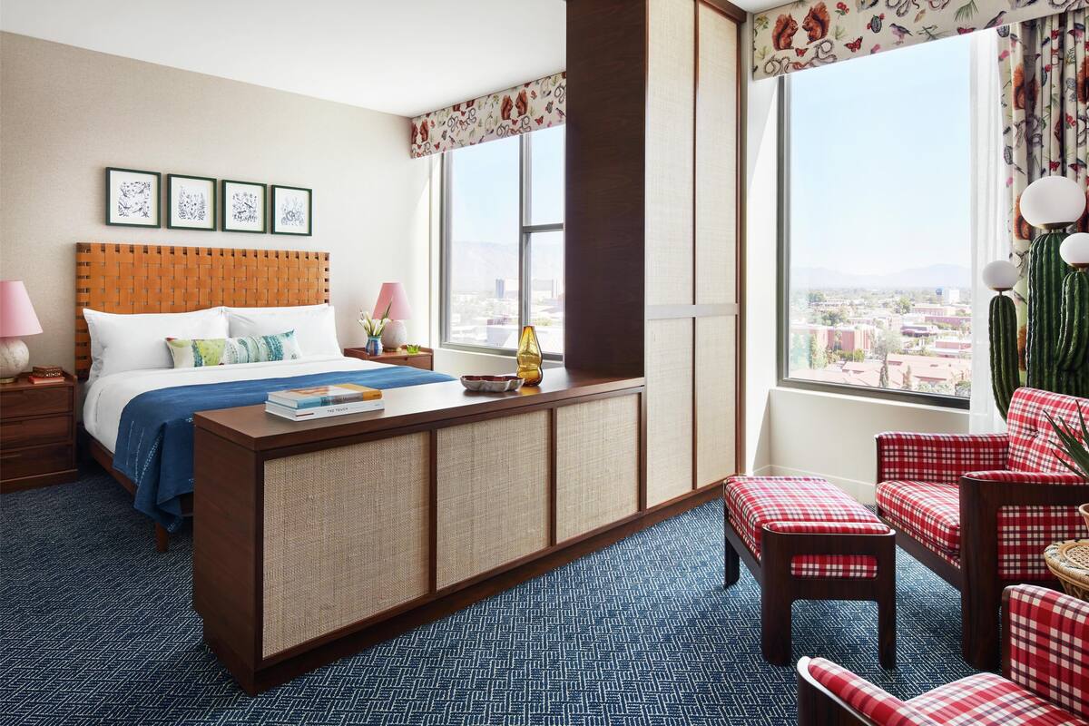 A hotel room with a bed, a desk, a chair, and a view of the city.