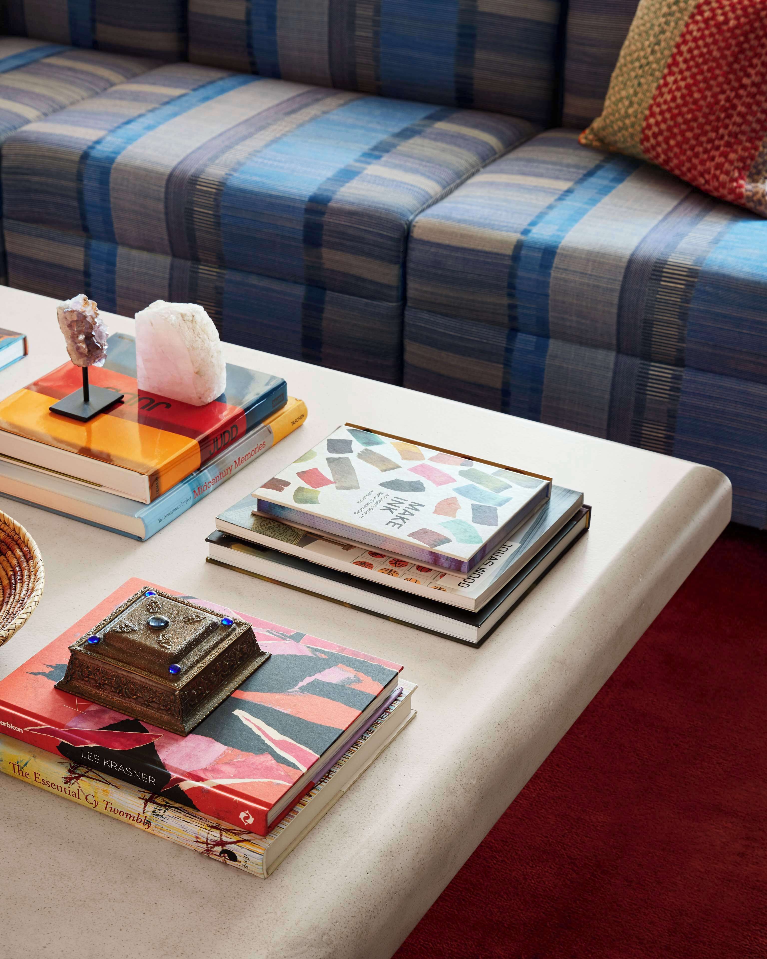 Una mesa ordenada con libros, adornos y un cojín sobre un sofá al fondo.