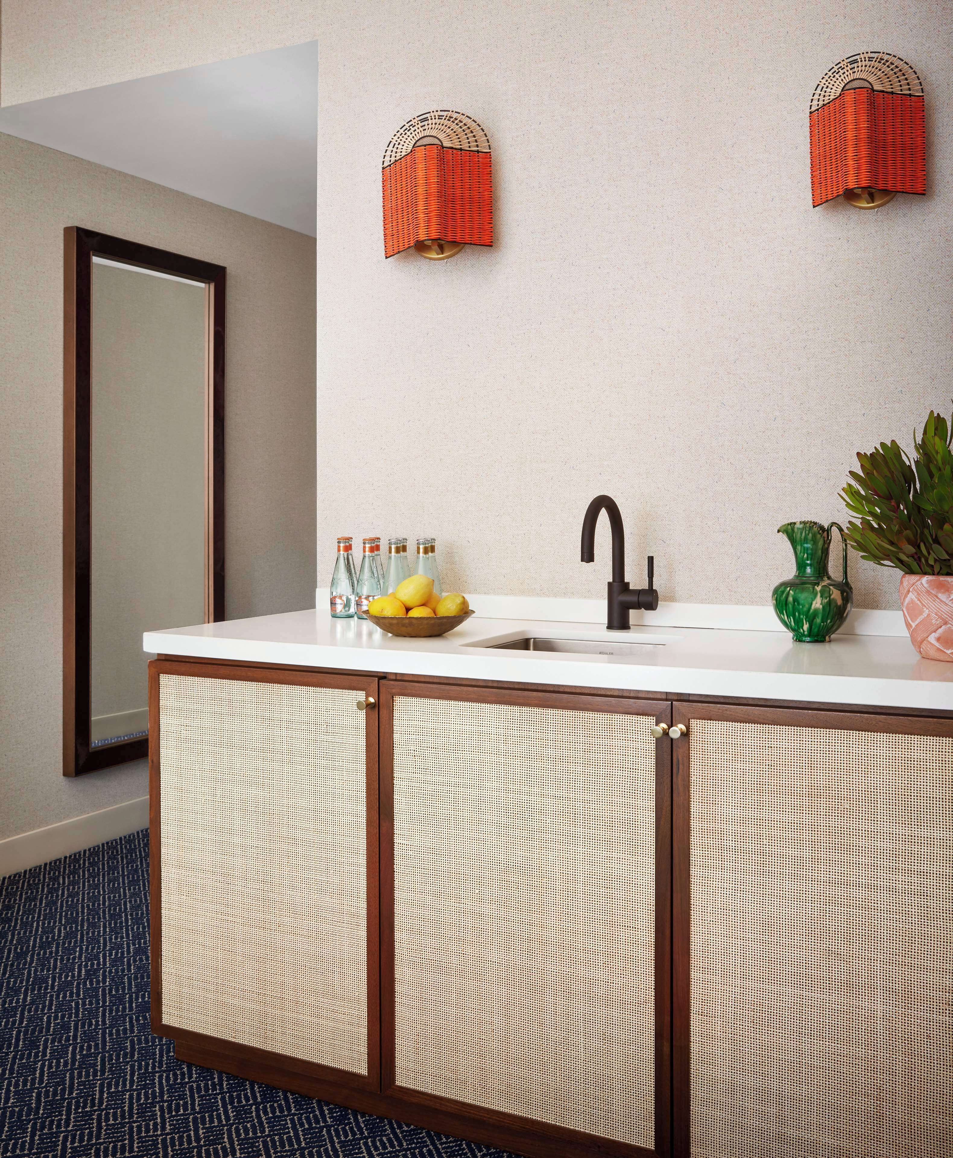 A bathroom with a white sink, a black faucet, and a mirror. There are two wall-mounted towel racks and a potted plant on the counter.