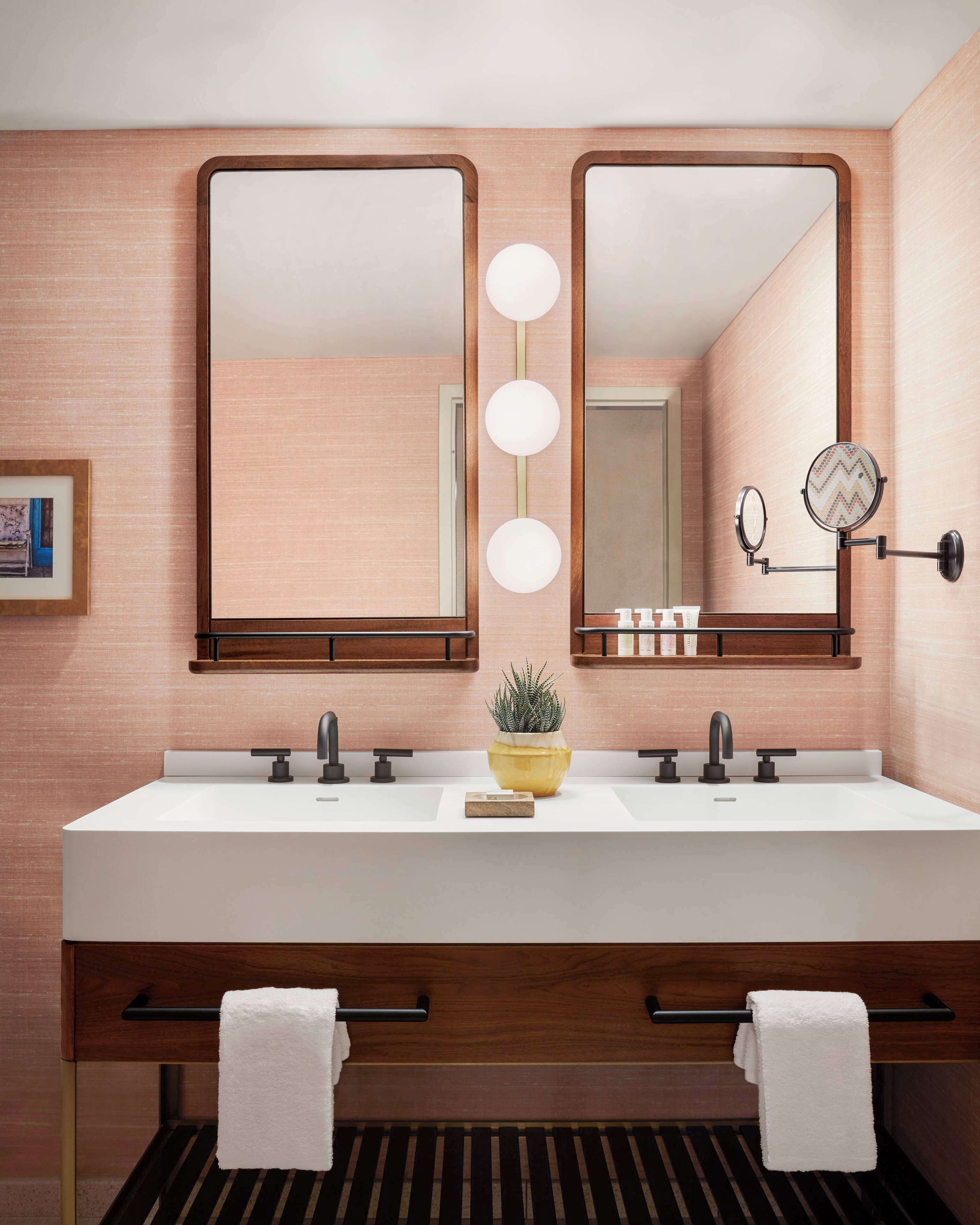 Une salle de bain moderne avec un double vasque, deux miroirs et une plante en pot.