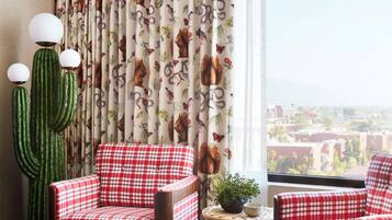 A room with a city view, featuring a red and white checkered sofa, a cactus, and curtains with a wildlife print.