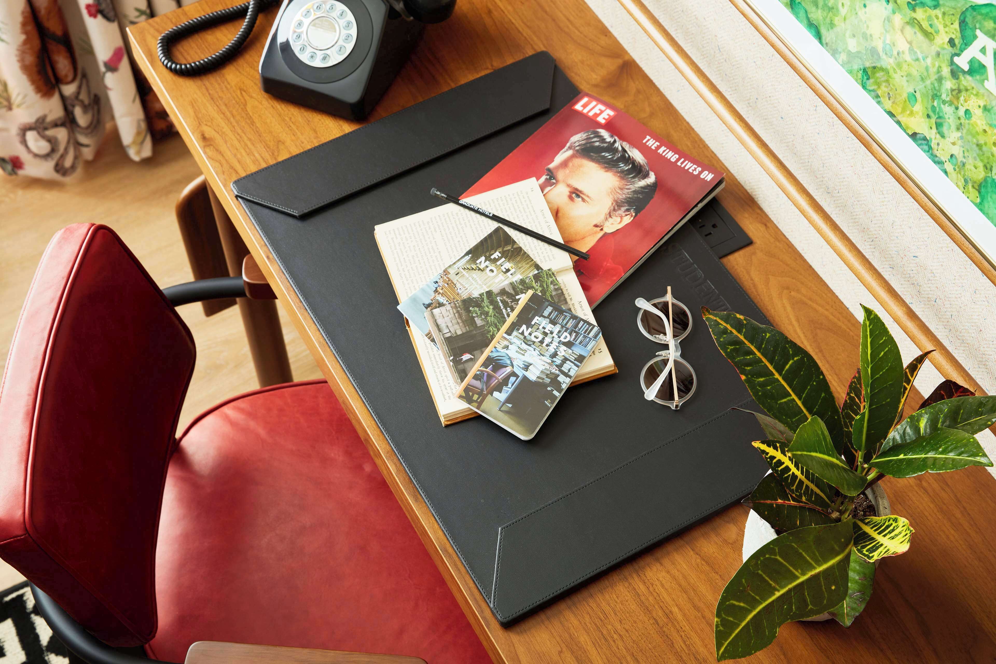 A desk with a leather chair, a black telephone, a Life magazine, a plant, and a pair of glasses.