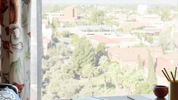 A desk with a rotary phone, a notebook, and a pencil, overlooking a cityscape with buildings and greenery.